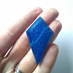 May include: A blue diamond-shaped resin cabochon with a sparkly finish. The cabochon has a white swirl pattern inside.