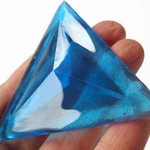 Puede incluir: Un gran prisma de cristal azul triangular con un diseño facetado.