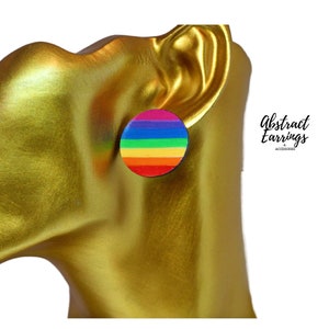 May include: A circular stud earring featuring a rainbow striped pattern. The earring is shown on a gold-coloured mannequin head. The text "Abstract Earrings" is visible in the upper right corner.