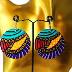 Könnte beinhalten: Ein Paar abstrakte Ohrringe mit farbenfrohem Design. Jeder Ohrring hat eine runde Form mit schwarzem Grund und türkisen, gelben, roten und violetten Mustern. Die Ohrringe sind an silbernen Haken befestigt. Der Text "Abstract Earrings" ist sichtbar.