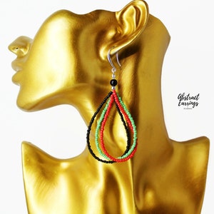 May include: A pair of dangle earrings with black, red, and green beads in a teardrop shape. The earrings are on a gold mannequin head. The text "Abstract Earrings" is visible in the image.