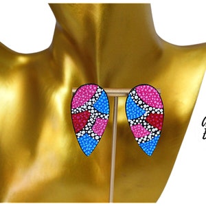 May include: A pair of abstract teardrop-shaped earrings with a pink, blue, and white dot pattern. The earrings are on a gold display stand. Abstract Earrings.