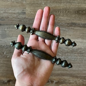 May include: Two antique-style cabinet knobs with ornate details. The knobs are made of metal and have a dark bronze finish.