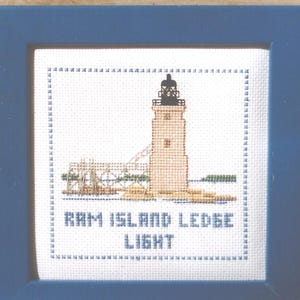 May include: A white cross-stitch embroidery of a lighthouse with the text "RAM ISLAND LEDGE LIGHT" underneath.