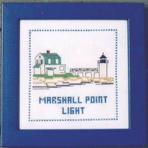 May include: A white cross-stitch embroidery framed in blue, depicting a lighthouse and a building with a red roof. The text "MARSHALL POINT LIGHT" is below the image.