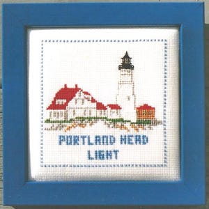 May include: Cross-stitch artwork depicting the Portland Head Light lighthouse in Maine. The white lighthouse has a red roof and is surrounded by other buildings. The text "Portland Head Light" is below the image.