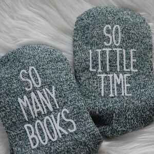 May include: A pair of green knitted socks with white text. One sock reads "So Many Books" and the other reads "So Little Time".