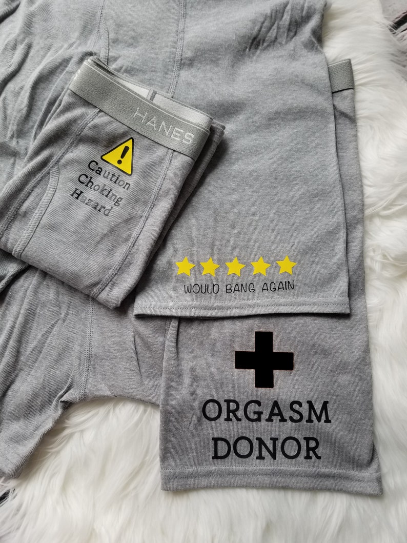Three designs shown on grey boxer briefs. Caution choking hazard with a caution symbol on the crotch area, orgasm donor with a cross on the left leg, and would bang again with 5 yellow stars above.