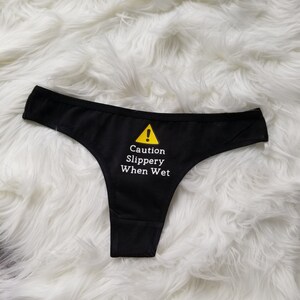 Another flat lay from further away of the cautions slippery when wet design on a black thong.