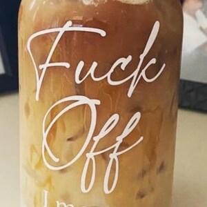 Customer photo showing 16oz glass with white text. Iced coffee is in the cup with a whipped cream topping and a glass straw.