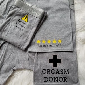 Three designs shown on grey boxer briefs. Caution choking hazard with a caution symbol on the crotch area, orgasm donor with a red cross on the left leg, and would bang again with 5 yellow stars above.