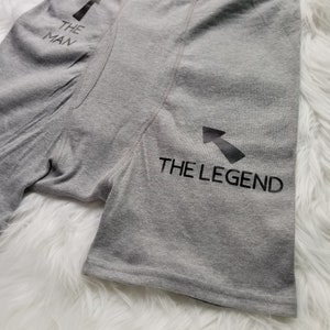 Grey boxer briefs lay flat on a white fuzzy rug. Design says The Man pointing up to the top of the underwear toward the person wearing them, then text saying the legend has an arrow pointing towards the crotch of the underwear.