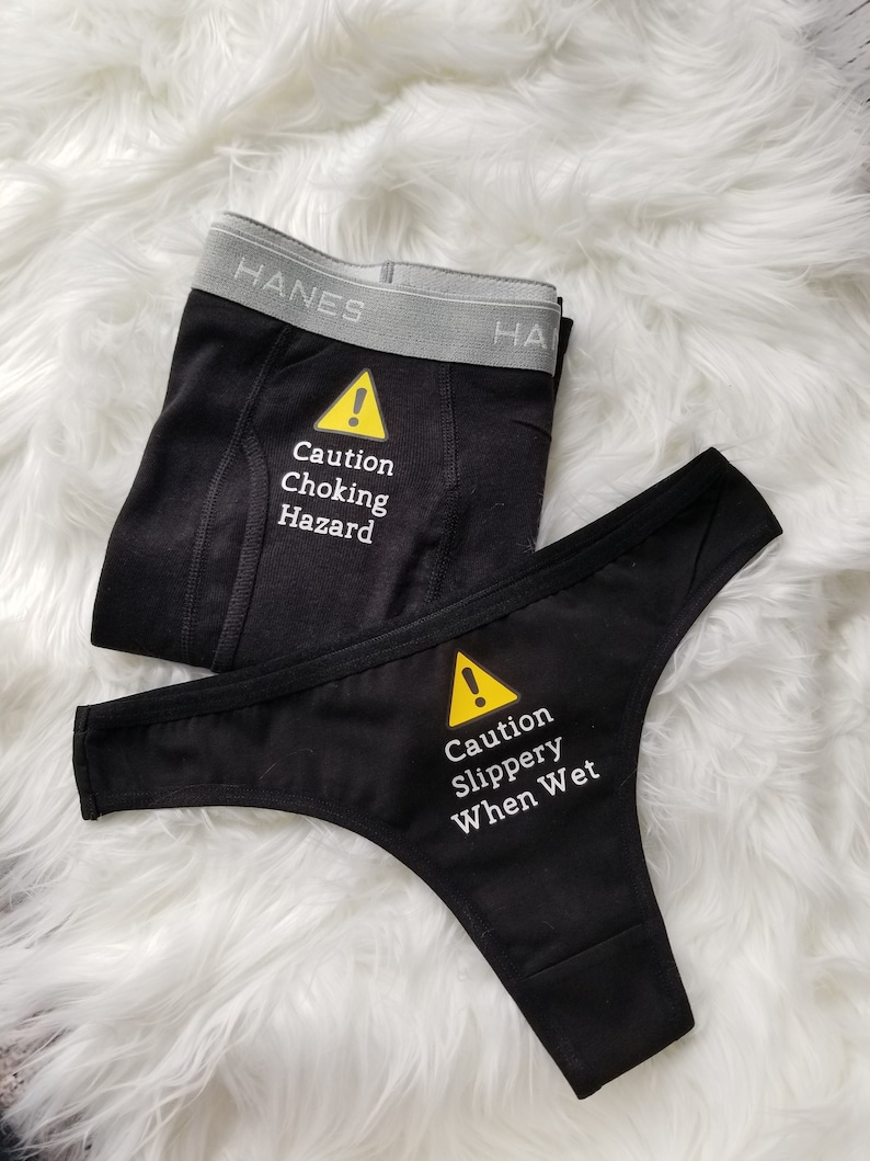 Matching boxer briefs and thong with saying on front. Men's says caution choking hazard, women's says caution slippery when wet. Women's comes in black or white thong or bikini, men's comes in black or grey boxer briefs.