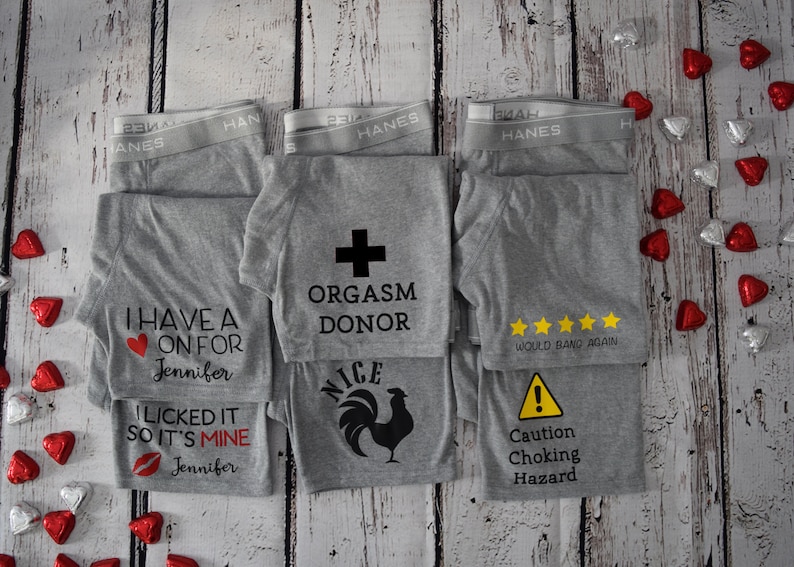 Six pairs of grey boxer briefs lay flat showing different designs available. Orgasm Donor with a cross above it, would bang again with 5 yellow stars above it, caution choking hazard with a caution symbol above it, and more.