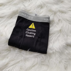 Caution choking hazard text with caution symbol on the crotch of a pair of black boxer briefs.
