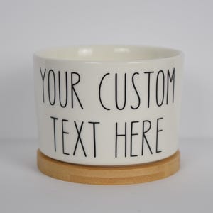 May include: White ceramic planter with a bamboo base. The planter has black text that reads "YOUR CUSTOM TEXT HERE".