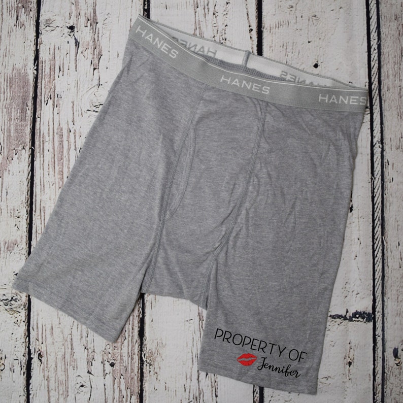 May include: Gray boxer briefs with the text "HANES" on the waistband and the text "PROPERTY OF Jennifer" with a red lip print on the bottom.