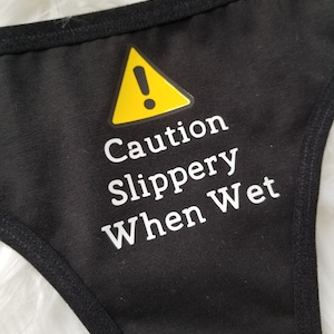 Close up of black thong with caution slippery when wet text in white with yellow caution sign above it.