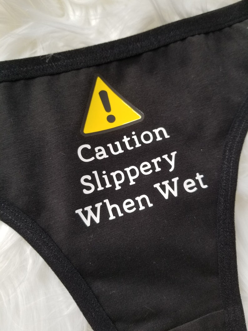 Close up of black thong with caution slippery when wet text in white with yellow caution sign above it.