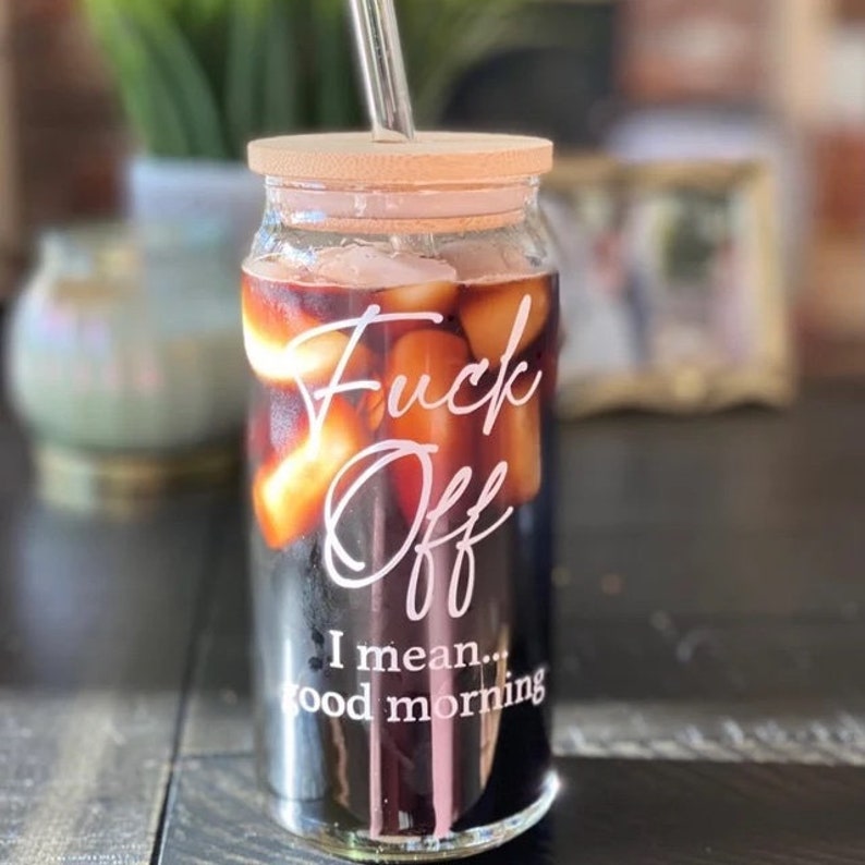 Customer photo of 20oz glass with white text. Shown with iced coffee or a dark iced tea. Cup has bamboo lid with glass straight straw.