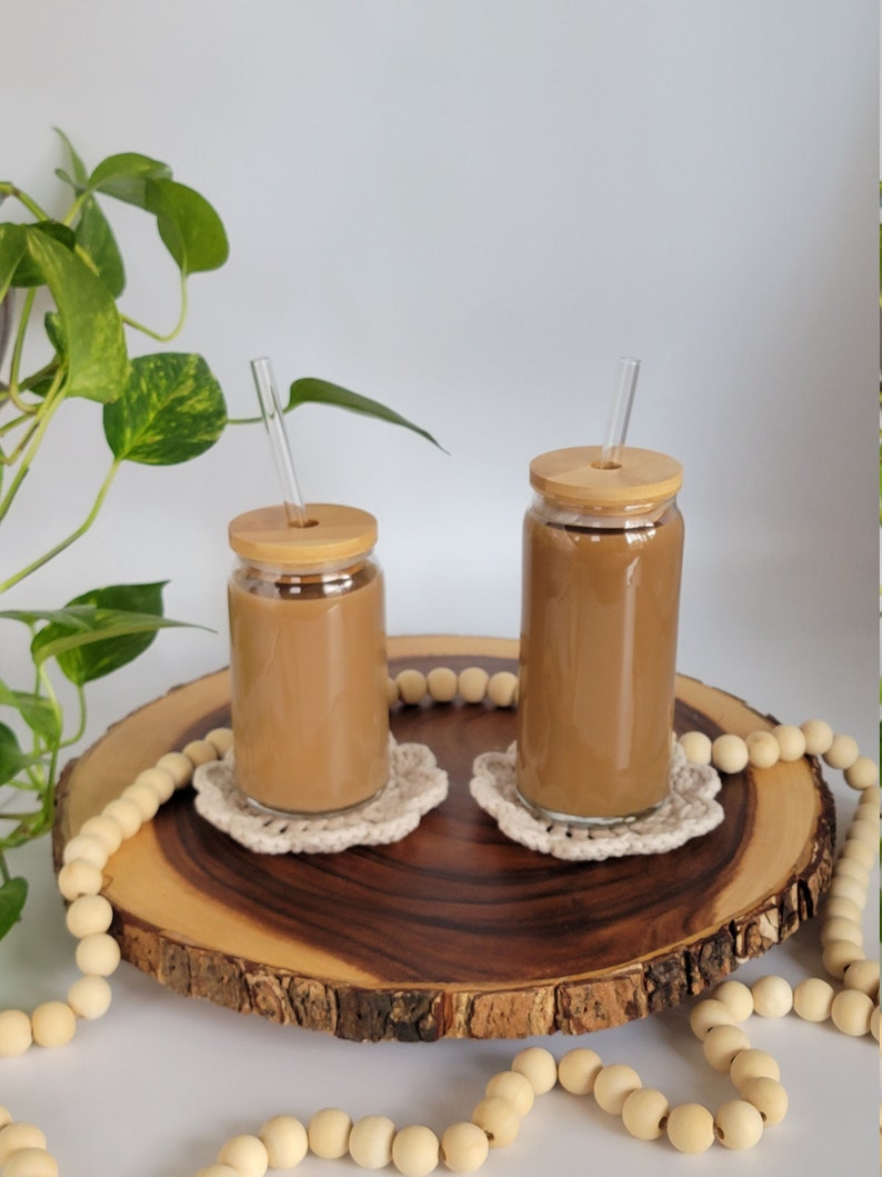 Size difference shown between 16oz and 20oz glasses. Glasses sit on a wooden slab, are filled with coffee, and have bamboo lids and straight glass straws.