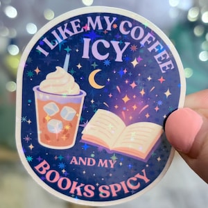 May include: A holographic sticker with the text "I like my coffee icy and my books spicy." The sticker features an iced coffee with whipped cream and an open book, set against a starry background.
