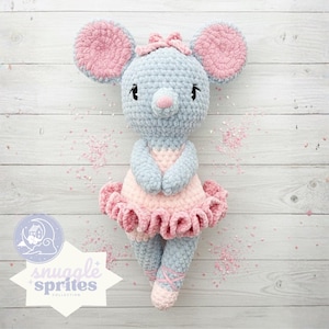 May include: A handmade crochet mouse doll in a ballerina outfit. The mouse is light blue with pink accents on the ears, bow, and tutu. The doll has embroidered eyes and a pink nose. The text "snuggle sprites collection" is in the lower left corner.