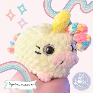 May include: A crocheted unicorn amigurumi toy with a yellow horn, pink nose, and rainbow yarn accents. The toy has large black eyes with glitter accents. The toy is being held in a hand against a pink background with rainbow stripes.