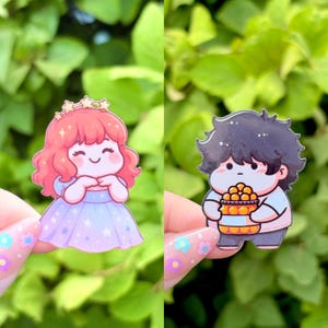 May include: Two cartoon stickers. One features a girl with red hair, a crown, and a blue dress. The other shows a boy with black hair holding a basket of oranges. Both stickers have a cute, chibi style.