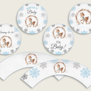 May include: Set of cupcake wrappers and toppers featuring a cute deer with a blue scarf in a winter wonderland scene with snowflakes. The toppers say "Mommy-to-be!" "Sweet Baby" and "Oh, Baby!"
