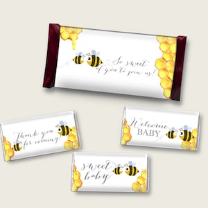 May include: A set of four chocolate bar wrappers featuring a bee and honeycomb design. The wrappers have different text, including "So sweet of you to join us!" and "Welcome Baby".