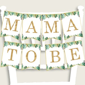 Puede incluir: Una pancarta blanca con follaje verde y letras doradas con brillo que deletrean "MAMA TO BE".