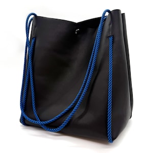May include: Black tote bag with bright blue rope handles and trim. The bag is made of a smooth material and has a simple, modern design. The bag is shown against a white background.