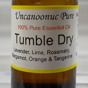 Könnte beinhalten: Eine braune Glasflasche mit ätherischem Öl und einem schwarzen Deckel. Auf dem Etikett steht "Uncanoonuc Pure" und "Tumble Dry". Zu den Inhaltsstoffen gehören Lavendel, Limette, Rosmarin, Bergamotte, Orange und Mandarine. Die Flasche enthält 15 ml.