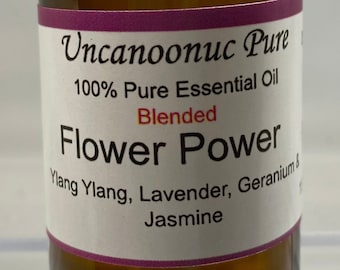 May include: A brown glass bottle of "Flower Power" essential oil. The label reads "Uncanoonuc Pure" and lists ingredients: Ylang Ylang, Lavender, Geranium & Jasmine. The bottle has a black cap and a purple label border.