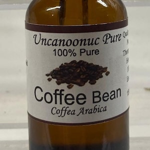Könnte beinhalten: Eine braune Glasflasche mit schwarzem Tropfer. Das Etikett lautet "Uncanoonuc Pure 100% Pure Coffee Bean Coffea Arabica". Die Flasche enthält eine dunkle Flüssigkeit, wahrscheinlich Kaffeeextrakt.