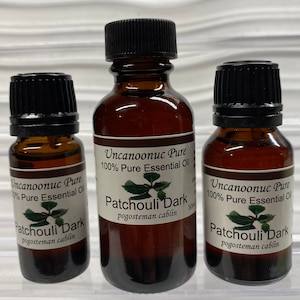 May include: Three amber glass bottles of essential oil with black caps. Each bottle has a white label with the text "Uncanoonuc Pure 100% Pure Essential Oil" and "Patchouli Dark". The bottles are of varying sizes, with the largest bottle containing 30ml.