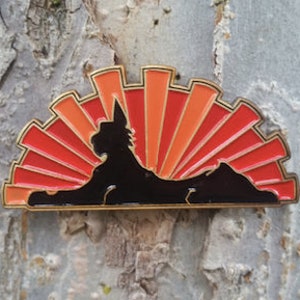 May include: A black silhouette of a cat sitting in front of a red and orange sunburst. The cat is facing the left side of the image. The sunburst is made of many thin, vertical lines. The image is a pin.