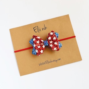 May include: Red, white and blue glitter bow with stars on a brown card with the text "Elii nik" and "www.EliiNik.etsy.com".