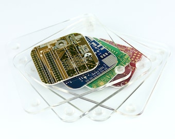 May include: A set of four square coasters made from recycled circuit boards, in gold, blue, green, and red. They are held in a clear acrylic holder, offering a unique and eco-friendly design. Each coaster is approximately 9 cm x 9 cm.