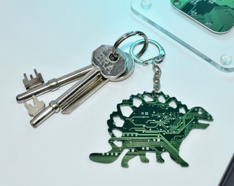 May include: A green circuit board dinosaur keychain with a silver key ring and two keys. The keys have the word "ERA" engraved on them.