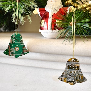 May include: Two Christmas ornaments shaped like bells, decorated with green and gold circuit boards, hanging from a Christmas tree with a Santa Claus figurine.