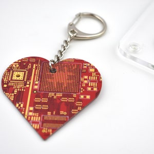 May include: A red heart-shaped keychain with a gold circuit board design. The keychain has a silver metal ring and chain.