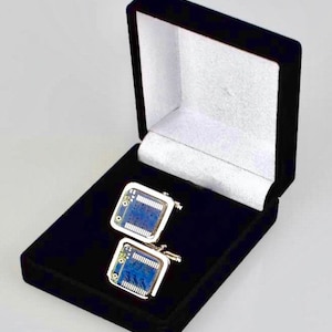 Könnte beinhalten: Ein Paar silberne Manschettenknöpfe mit einem blauen Schaltkreisdesign, präsentiert in einer schwarzen Samtbox.