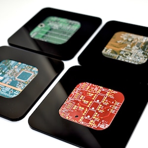 May include: Four black square coasters with a clear window in the center. Each window displays a different colored circuit board.