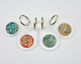 May include: Four keychains with clear plastic teardrop-shaped charms. Each charm features a round, colorful printed image of a circuit board.