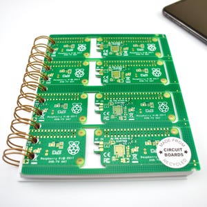 Puede incluir: Una libreta verde con encuadernación en espiral. La cubierta está hecha de placas de circuito recicladas y tiene el texto "Raspberry Pi 2017 DVB-TV HAT" impreso en ella. La libreta también tiene el texto "MADE FROM CIRCUIT BOARDS RECYCLED" impreso en la cubierta.