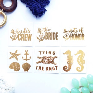 May include: Set of six gold foil temporary tattoos with nautical and wedding themes. The tattoos include the phrases "bride's crew", "the bride", "mate of honor", and "tying the knot".  There are also images of an anchor, a starfish, a seashell, and a seahorse.