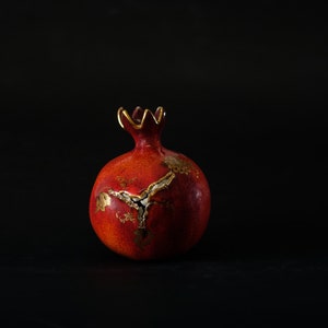 Peut inclure: Une grenade en céramique rouge avec des détails en feuille d'or. La grenade est un symbole traditionnel d'abondance et de prospérité.