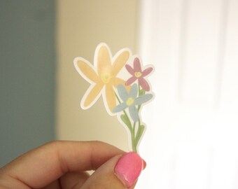 May include: A sticker depicting three stylized flowers in yellow, pink, and blue, with green stems and leaves. The sticker has a white border. The design is simple and cheerful.
